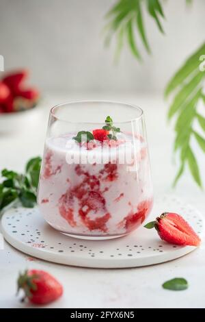 smoothie aux fraises maison, cocktail dans un verre décoré de tranches de fraises fraîches et de menthe sur fond gris avec des feuilles vertes. régime ou Banque D'Images