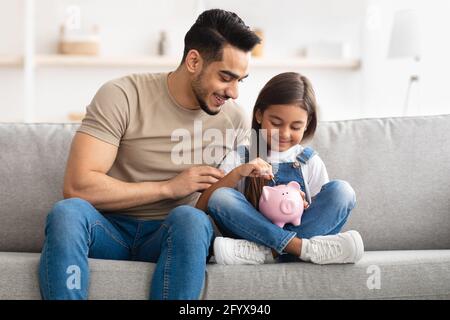 Une petite fille et un père économisent de l'argent dans une banque de porc Banque D'Images