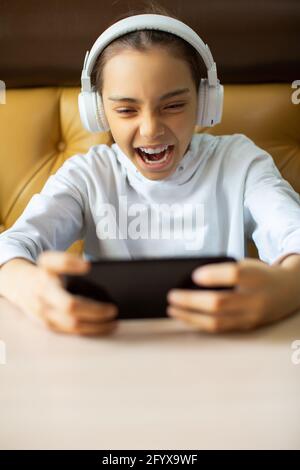 Photo verticale d'une adolescente jouant à un jeu en ligne sur son smartphone. Elle crie émotionnellement dans une tentative de gagner le tour. Banque D'Images