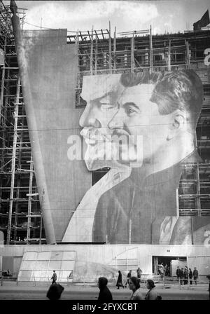 Une grande affiche avec des portraits des dirigeants politiques russes Vladimir Lénine et Joseph Staline pour le défilé du jour de mai pend sur l'échafaudage d'un bâtiment en construction, Moscou, Russie, 1934.(Photo de Burton Holmes) Banque D'Images