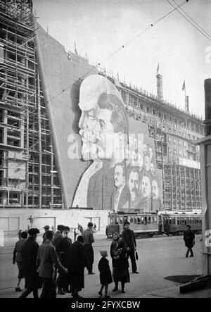 Une grande affiche avec des portraits des dirigeants politiques russes Vladimir Lénine, Joseph Staline et d'autres pour le défilé du jour de mai pend sur l'échafaudage d'un bâtiment en construction, Moscou, Russie, 1934.(Photo de Burton Holmes) Banque D'Images