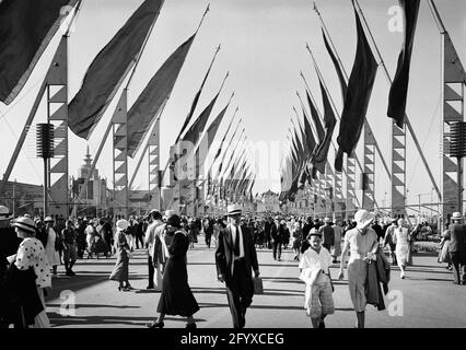 Les Fairgoers qui visitent l'exposition internationale Century of Progress, également connue sous le nom de Chicago World's Fair, se promèdent le long de l'Avenue of Flags, Chicago, Illinois, 1933. L'aquarium Shedd est visible au loin. (Photo de Burton Holmes) Banque D'Images