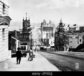 Vue vers l'est en descendant California Street, environ de l'intersection à Stockton Street, San Francisco, Californie, 1915. La tour de la cathédrale Sainte-Marie et le bâtiment Sing Chong, à l'intersection de l'avenue Grant, sont visibles sur la gauche. La tour de l'horloge du Ferry Building est visible au loin. (Photo de Burton Holmes) Banque D'Images