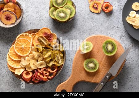 Fabrication de chips de fruits maison de prunes, kiwi, pêche, prune, orange sur fond de pierre grise, séchage à la maison. En-cas végétalien gratuit. Vue de dessus. Banque D'Images