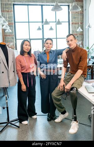 Groupe de jeunes designers confiants de vêtements debout devant de la caméra dans l'atelier Banque D'Images