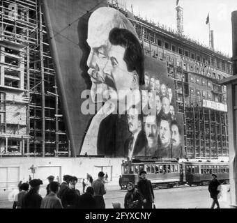 Une grande affiche avec des portraits des dirigeants politiques russes Vladimir Lénine, Joseph Staline et d'autres pour le défilé du jour de mai pend sur l'échafaudage d'un bâtiment en construction, Moscou, Russie, 1934.(Photo de Burton Holmes) Banque D'Images