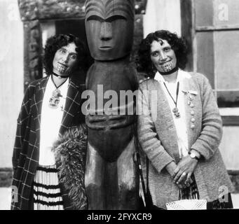 Des jumeaux maoris se dressent de part et d'autre d'une statue traditionnelle en bois, Rotorua, Nouvelle-Zélande, 1917. (Photo de Burton Holmes) Banque D'Images