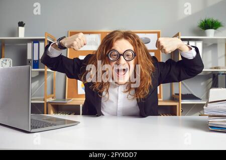 Drôle de travailleur de bureau assis au bureau et de flexion des muscles heureux pour commencer une journée de travail Banque D'Images