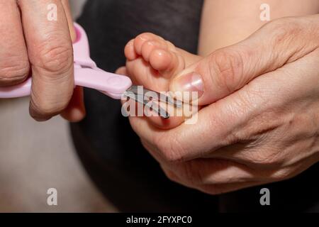 Main de maman tenant des petits ciseaux pour couper les ongles sur le pied du petit bébé. Banque D'Images