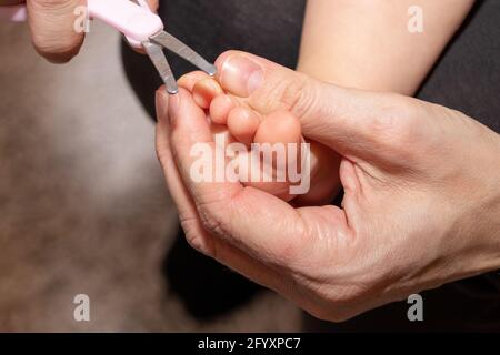 Main de maman tenant des petits ciseaux pour couper les ongles sur le pied du petit bébé. Banque D'Images