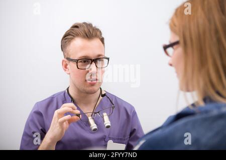 Jeune dentiste de sexe masculin parlant à son patient de sexe féminin Banque D'Images