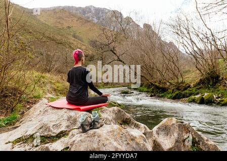 Corps complet de la jeune femme assise avec les jambes croisées côte rocheuse de la rivière Banque D'Images