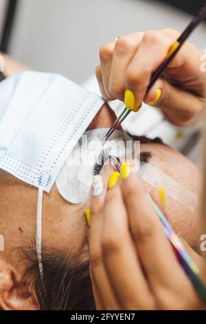 Rognez un cosmétologue méconnaissable à l'aide d'une pince à épiler en appliquant de faux cils pour l'extension à l'œil du client dans le salon Banque D'Images