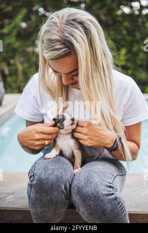 Jeune femme blonde embrassant Border Collie chiot avec les yeux fermés sur la véranda en journée Banque D'Images