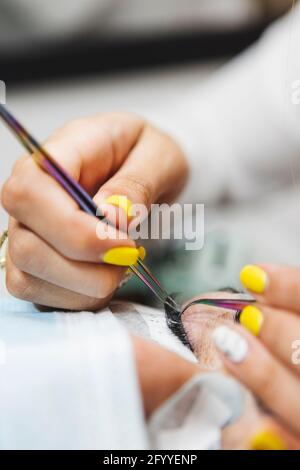 Rognez un cosmétologue méconnaissable à l'aide d'une pince à épiler en appliquant de faux cils pour l'extension à l'œil du client dans le salon Banque D'Images
