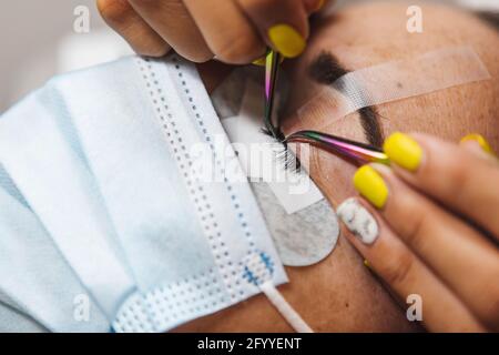 Rognez un cosmétologue méconnaissable à l'aide d'une pince à épiler en appliquant de faux cils pour l'extension à l'œil du client dans le salon Banque D'Images