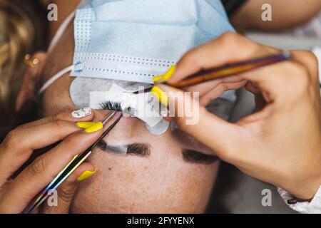 Grand angle de récolte cosmétologue méconnaissable avec des pinces à épiler en appliquant de faux cils pour extension sur l'œil du client en salon Banque D'Images