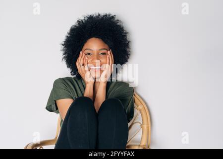 Une femme afro-américaine positive regarde la caméra sur une chaise en bois Banque D'Images