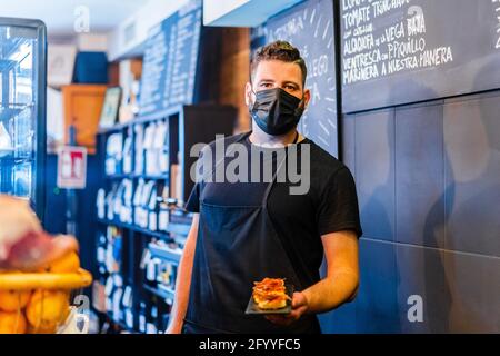 Joyeux homme ethnique avec un plateau de démonstration de barbe avec des aliments savoureux tout en regardant la caméra dans le restaurant Banque D'Images