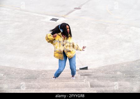 D'en haut, une femme afro-américaine dansant debout contre l'escalier et écouter de la musique avec un casque Banque D'Images