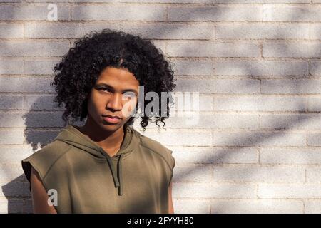 Africain américain adolescent avec la coiffure afro portant des vêtements décontractés se tenir à la lumière du soleil contre un mur de briques Banque D'Images