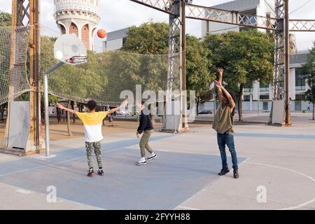 Tout le corps de concentré multiethnique teen amis dribbling ball pendant entraînement au basket-ball sur le terrain de sport dans le parc de la ville Banque D'Images