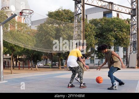 Tout le corps de concentré multiethnique teen amis dribbling ball pendant entraînement au basket-ball sur le terrain de sport dans le parc de la ville Banque D'Images