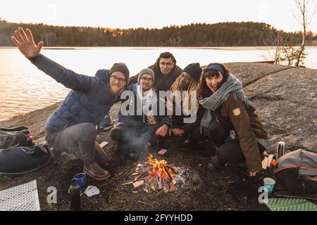 Un groupe d'amis multiethniques souriants s'embrassant les uns les autres feu de camp sur la côte de l'étang Banque D'Images