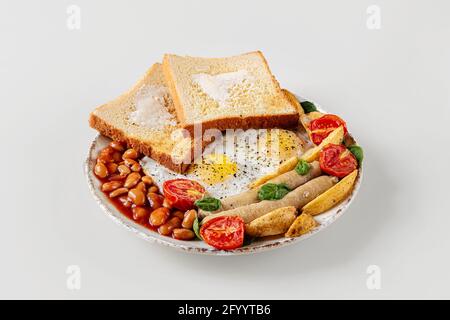 délicieux petit déjeuner frais sur une assiette isolée sur fond blanc. savoureux œufs frits, saucisses viennoises, tomates cerises et épinards Banque D'Images