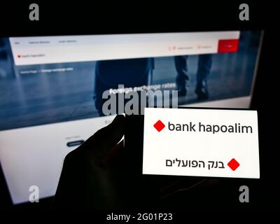 Personne tenant un smartphone avec le logo de la société financière israélienne Bank Hapoalim BM à l'écran en face de la page Web d'affaires. Mise au point sur l'affichage du téléphone. Banque D'Images