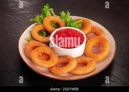 Calamars anneaux. Rondelles de calmars frite avec feuilles de laitue et ketchup sur fond noir Banque D'Images