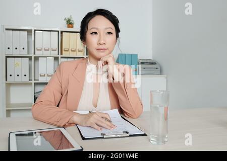 Une femme pensive, responsable des ressources humaines, rédige la liste des exigences du poste Banque D'Images