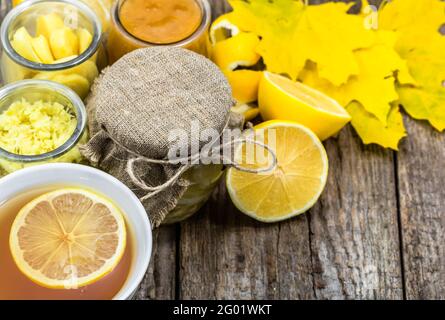 Thé au citron sur fond de bois rustique. Ingrédients dans des pots en verre, gingembre et miel. Concept avec feuilles d'automne. Banque D'Images