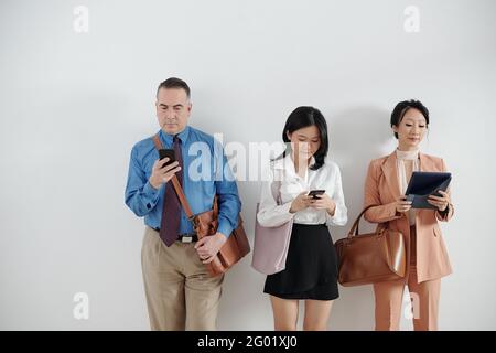 Candidats en file d'attente, en attente d'un entretien d'embauche et en consultant les médias sociaux sur smartphones et tablettes Banque D'Images