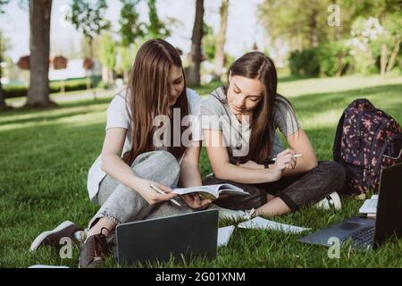 Deux étudiantes sont assises dans le parc sur l'herbe avec des livres et des ordinateurs portables, étudiant et préparant pour les examens. Enseignement à distance. Sélection douce Banque D'Images