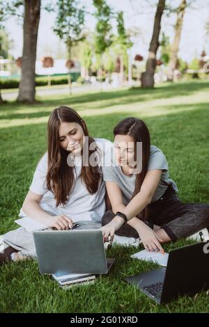 Deux étudiantes sont assises dans le parc sur l'herbe avec des livres et des ordinateurs portables, étudiant et préparant pour les examens. Enseignement à distance. Sélection douce Banque D'Images