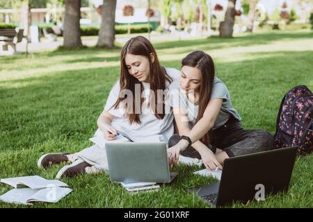 Deux étudiantes sont assises dans le parc sur l'herbe avec des livres et des ordinateurs portables, étudiant et préparant pour les examens. Enseignement à distance. Sélection douce Banque D'Images