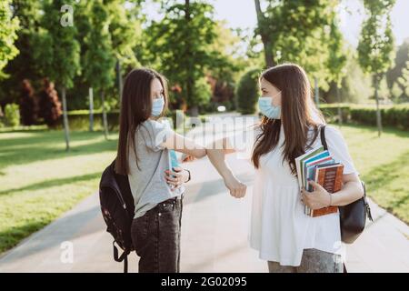 Deux étudiantes en masques médicaux protecteurs accueillent leurs coudes lorsqu'elles se rencontrent sur le campus. Enseignement à distance. Mise au point sélective douce. Banque D'Images