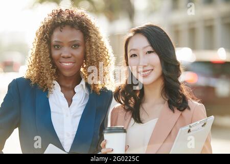 Portrait de jeunes femmes entrepreneures souriantes se tenant à l'extérieur le jour ensoleillé, buvant un café à emporter et regardant l'appareil photo Banque D'Images
