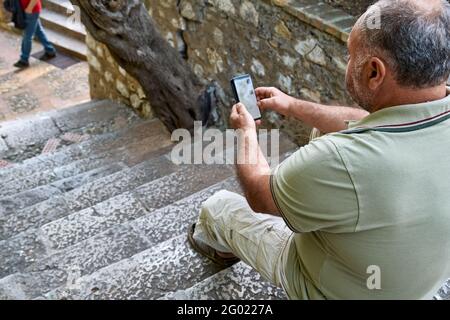 Un homme d'âge moyen souriant utilise un smartphone seul sur le Escalier en pierre dans le parc.gadgets et technologies modernes Banque D'Images