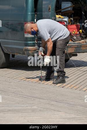 Un employé du département des parcs de la ville de New York ajuste et fixe des lattes sur la promenade de Coney Island, Brooklyn, New York. Banque D'Images