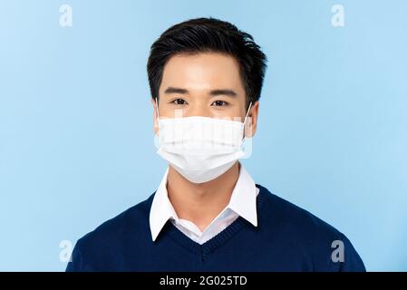 Portrait en gros plan d'un jeune homme asiatique élégant portant un médecin masque facial isolé sur fond bleu clair Banque D'Images