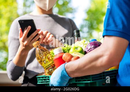 Femme client portant un masque de contrôle épicerie qui a commandé en ligne et livré par livreur à la maison, service de livraison de nourriture dans les temps de COVI Banque D'Images