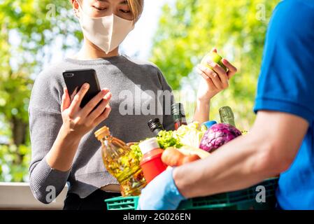 Femme client portant un masque de contrôle épicerie qui a commandé en ligne et livré par livreur à la maison, service de livraison de nourriture dans les temps de COVI Banque D'Images