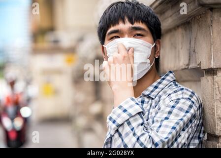 Jeune homme asiatique portant un masque facial à l'extérieur de la ville Pendant la pandémie de COVID-19 Banque D'Images