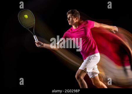 Un homme, un joueur de tennis masculin s'entraîner isolé dans un éclairage néon mixte sur fond sombre. Concept de sport, compétition d'équipe. Banque D'Images