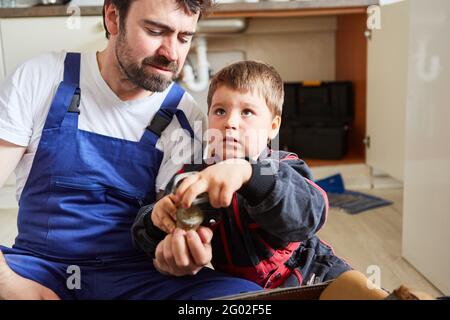 Un garçon avec une vanne d'arrêt cassée dans l'évier de cuisine aide son père l'assemble Banque D'Images