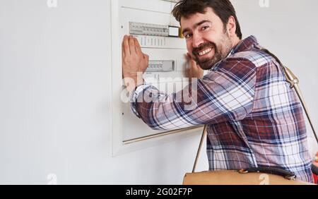 Homme souriant comme électricien ou homme de main à la jonction boîte avec fusibles Banque D'Images