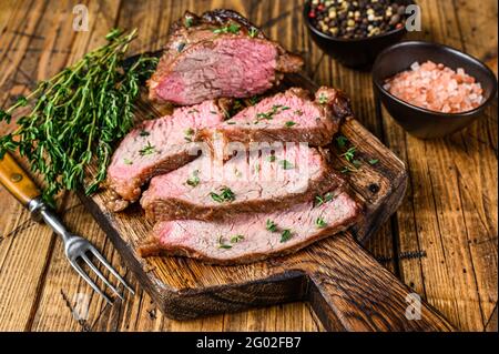 Tranches rares de rôti de boeuf sirloin à trois pointes steak bbq sur une planche à découper en bois. fond en bois. Vue de dessus Banque D'Images
