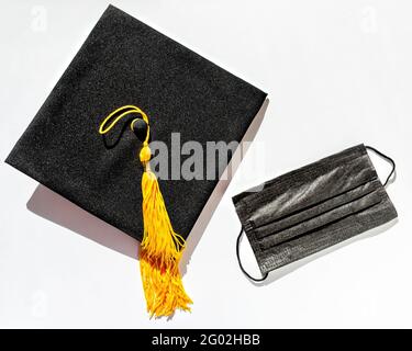 Casquette de troisième cycle noire avec pampille jaune et masque de protection sur fond blanc, protection contre le virus pendant l'étude, obtention d'un diplôme en nouveau reali Banque D'Images